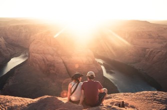 man and woman watching sunset over a cliff